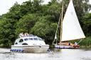 A hire cruiser passes a yacht in the Norfolk Broads